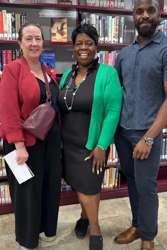 Mira Prinz-Arey, Deborah "Miss Debbie" Oriol, and Elisha Dorsey standing together in front of the shelves inside the West Bergen Branch.