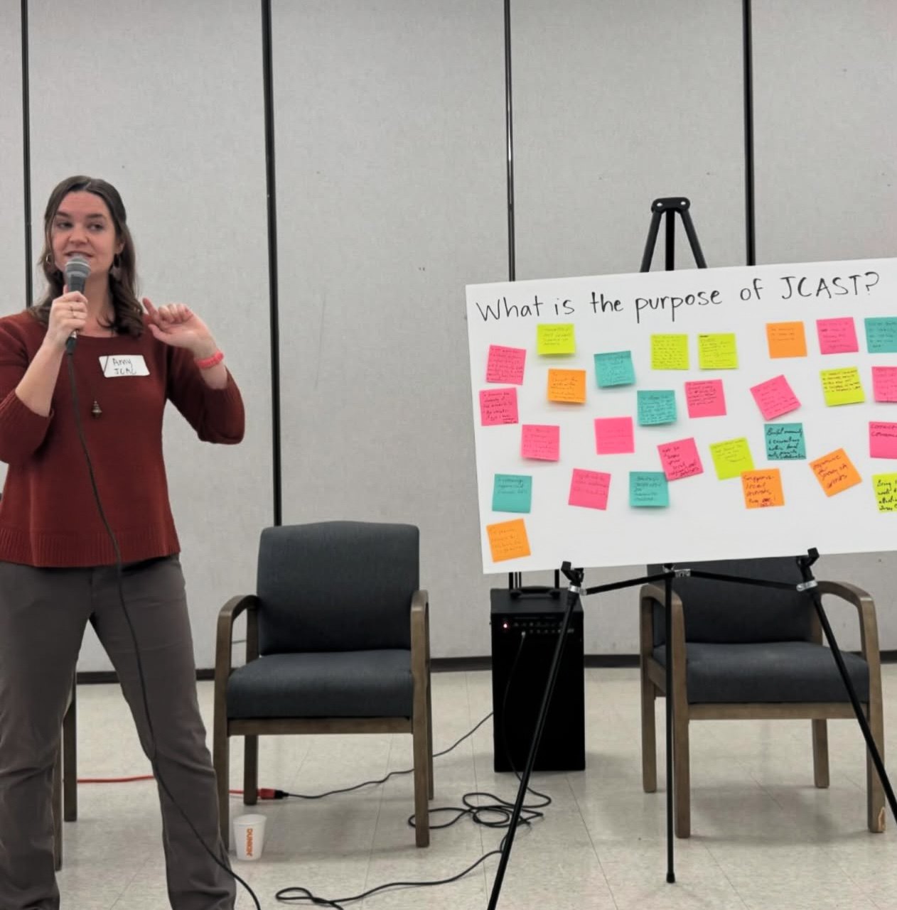A facilitator speaking beside an easel board covered in handwritten sticky notes.